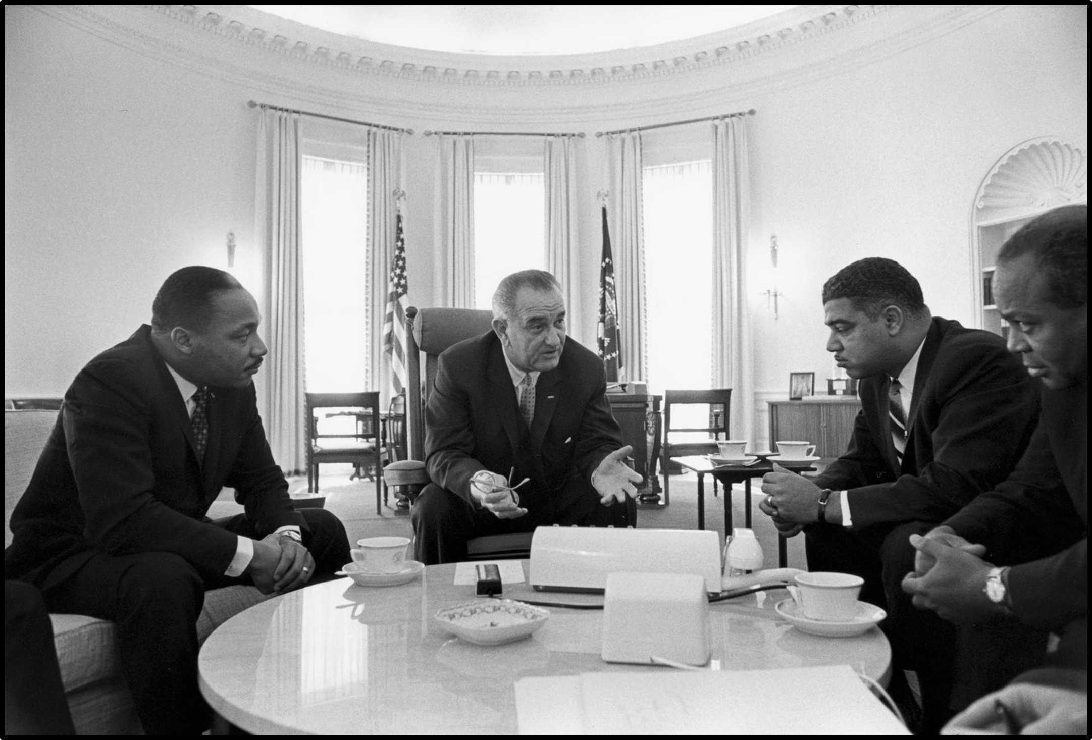 Lyndon B. Johnson sits at a table in the Oval Office with Martin Luther King, Jr., Whitney Young, and James Farmer.