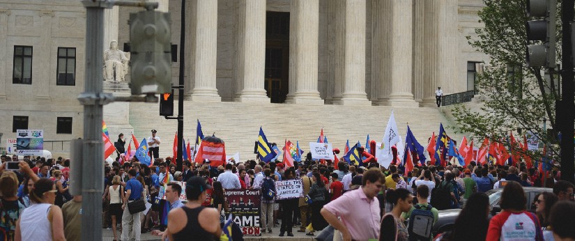 Group of people standing in front of a building. Some people are holding signs.