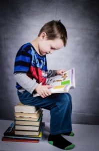 Young Child sitting on a stack of books reading a book