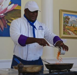 A man demonstrating cooking by dumping vegetables into a pan.