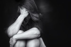 Black and white image of a young woman crying and covering her face useful to illustrate stress, depression or domestic violence