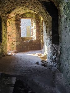A long tunnel that leads to a window inside of a stone castle. 