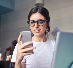 A woman sitting at a laptop and looking at her phone