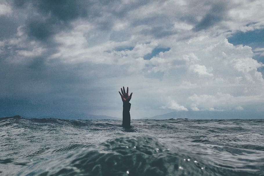 Photo of person hand reaching out above body of water.