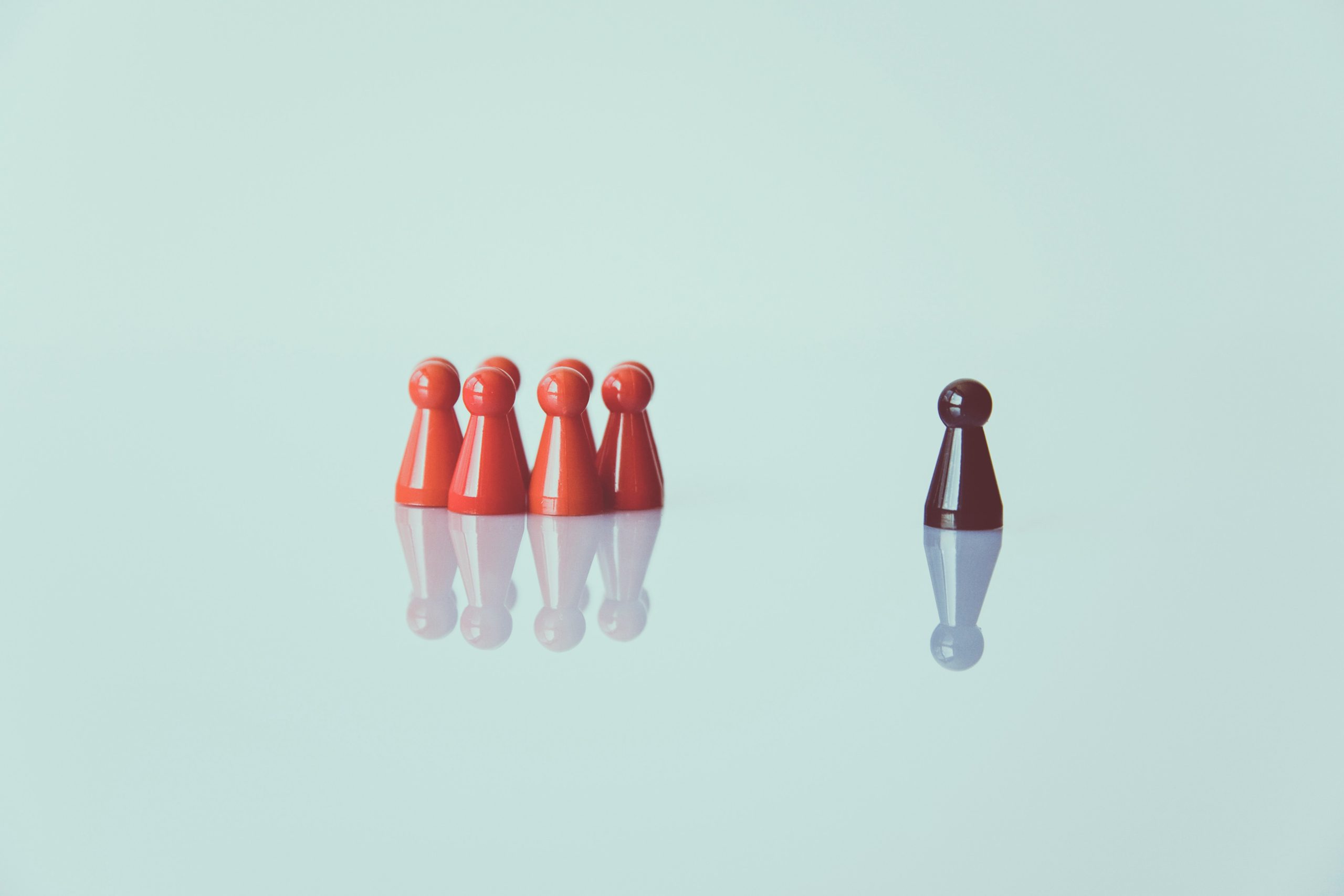 Group of game pieces and one game piece standing alone on a reflective surface. Boss and employee or exclusion of a person because of their appearance?