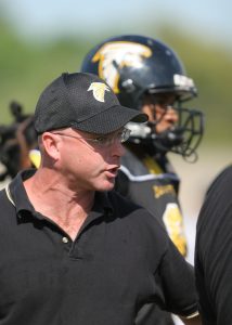 A football coach stands on the sidelines.