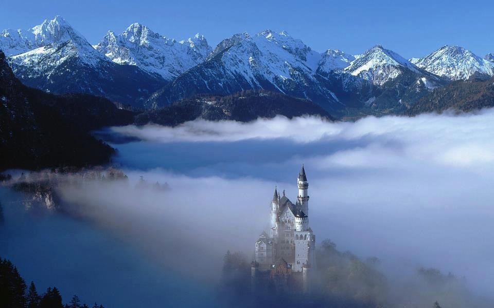 Photo of the "fairytale castle" of Neuschwanstein, a turreted castle with snow covered mountains in the background